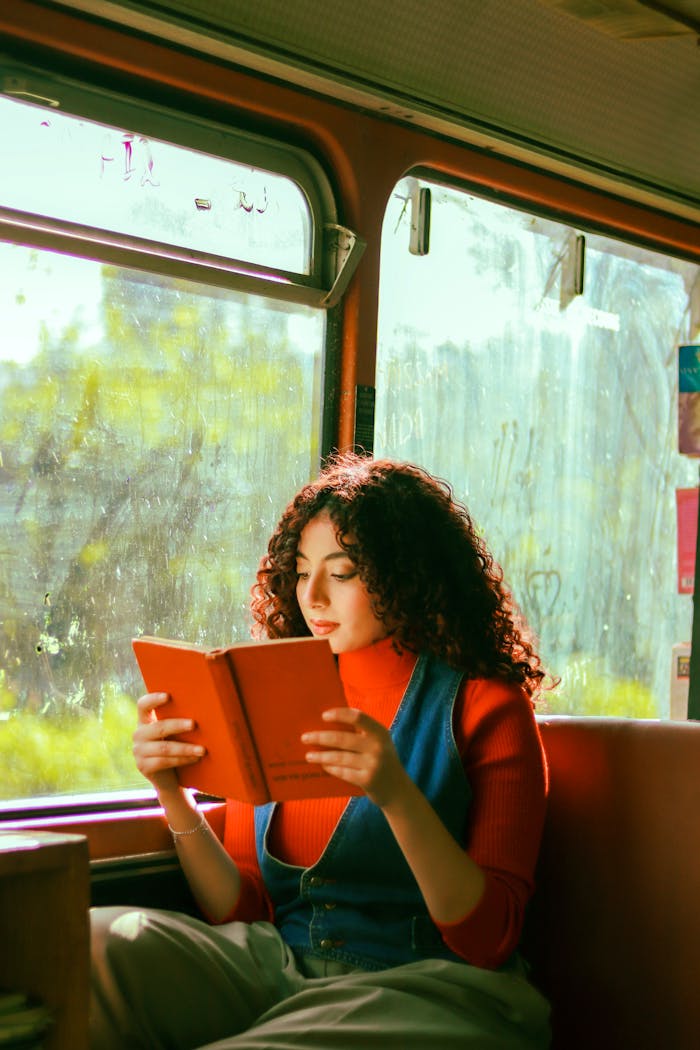 Young woman reading a book while traveling on a bus, bathed in natural light.