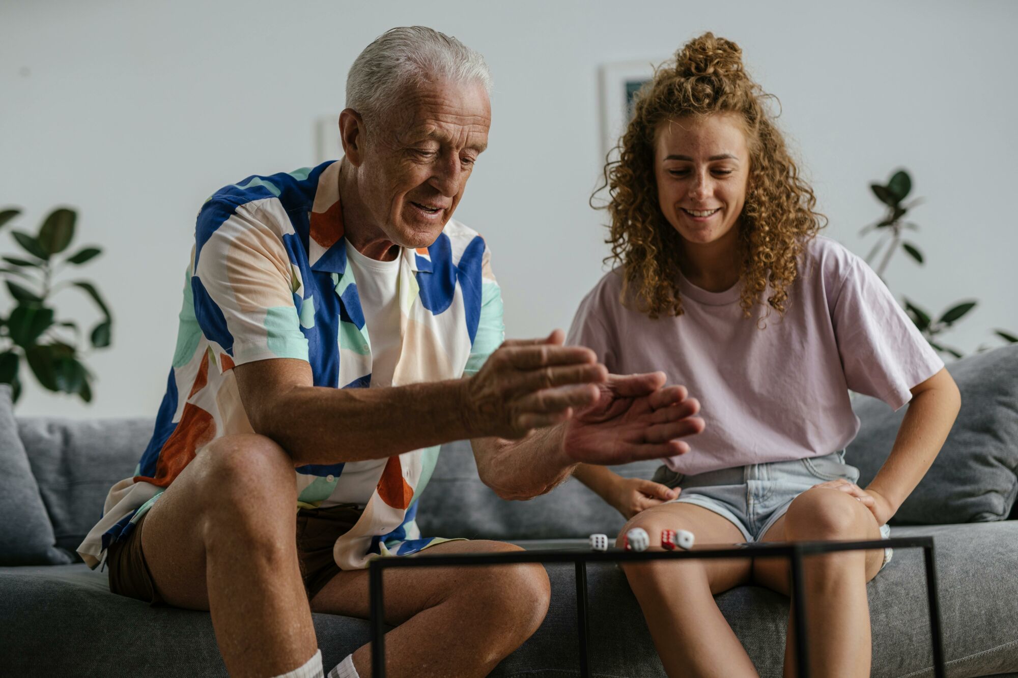 A senior man and young woman enjoying a dice game together on the couch.