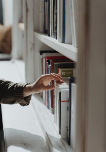pexels-photo-4855351 A hand reaches out to select a book from a well-arranged indoor bookshelf.